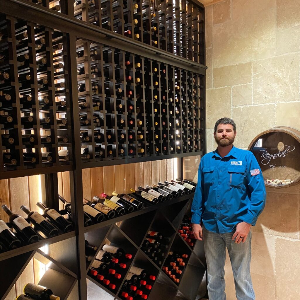 Greg Byrus standing in front of completed wine cellar with wine bottles.